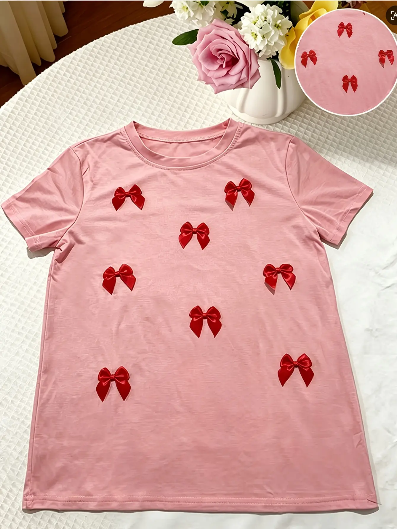 Pink crew-neck T-shirt with red bow appliques laid flat